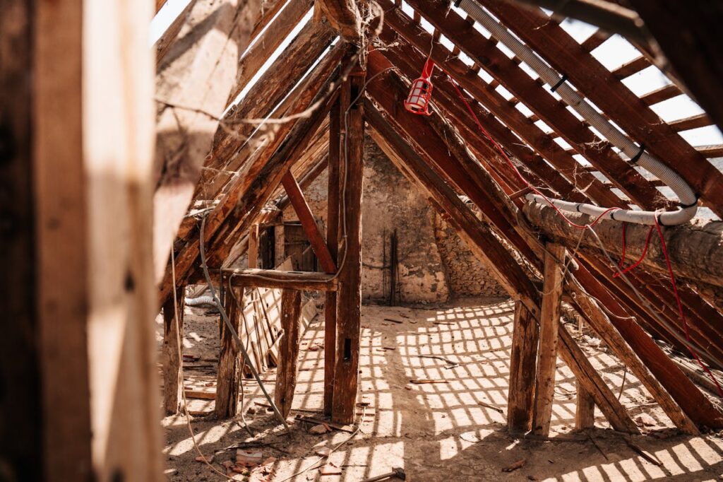 Interior view of wooden framing and rafters in a partially constructed attic space, highlighting a rustic and textured structure.