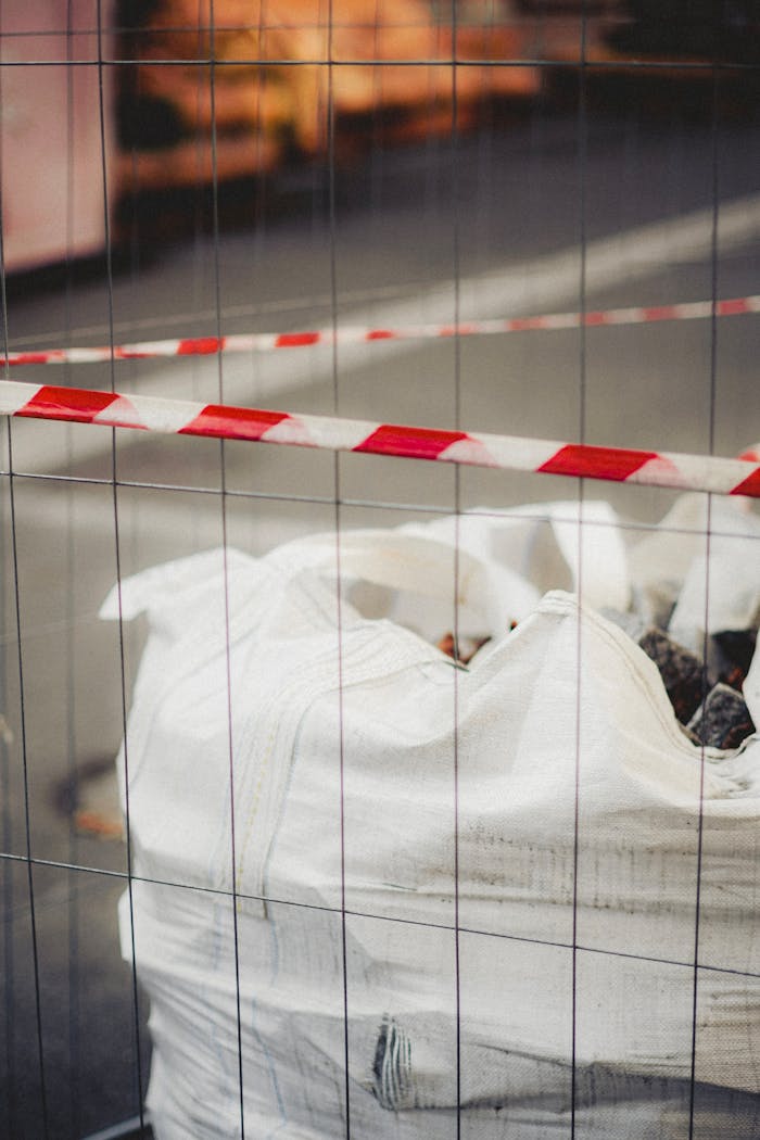Close-up of debris-filled sack at construction site enclosed by red and white tape.